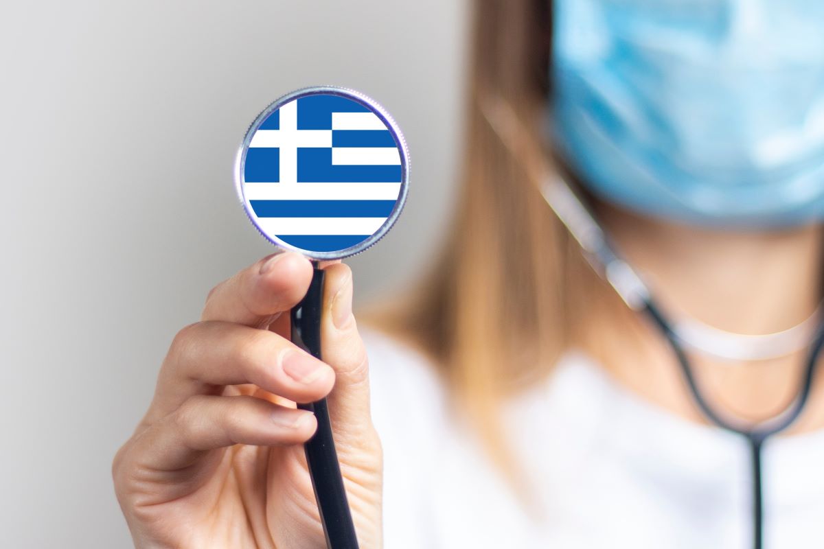 Greek doctor holding up a stethoscope with the Greek flag.